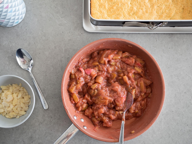 ba blacie patelnia z podgotowanym rabarbarem obok w formie spód do ciasta oraz miseczka z płatkami migdałów