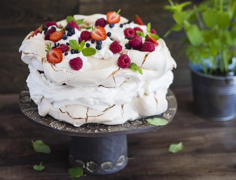 Letni tort bezowy przełożony śmietankowym kremem, udekorowany owocami, położony na paterze - Wszystkiego Słodkiego