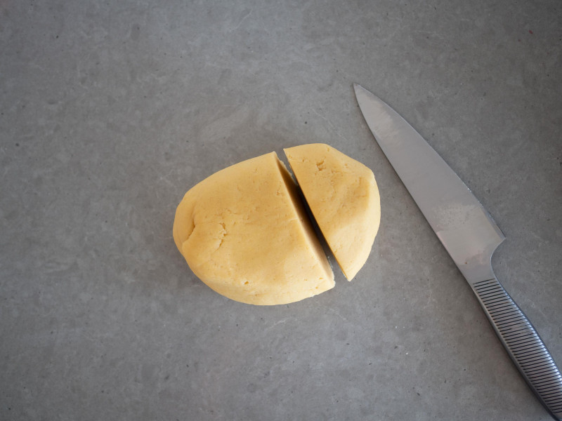 zagniecione ciasto kruche na blacie kuchennym uformowane w kulę i przekrojone nożem na dwie części - mniejszą i większą