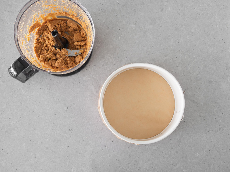 Ciasteczkowa masa w malakserze. Obok tortownica wyłożona papierem do pieczenia.