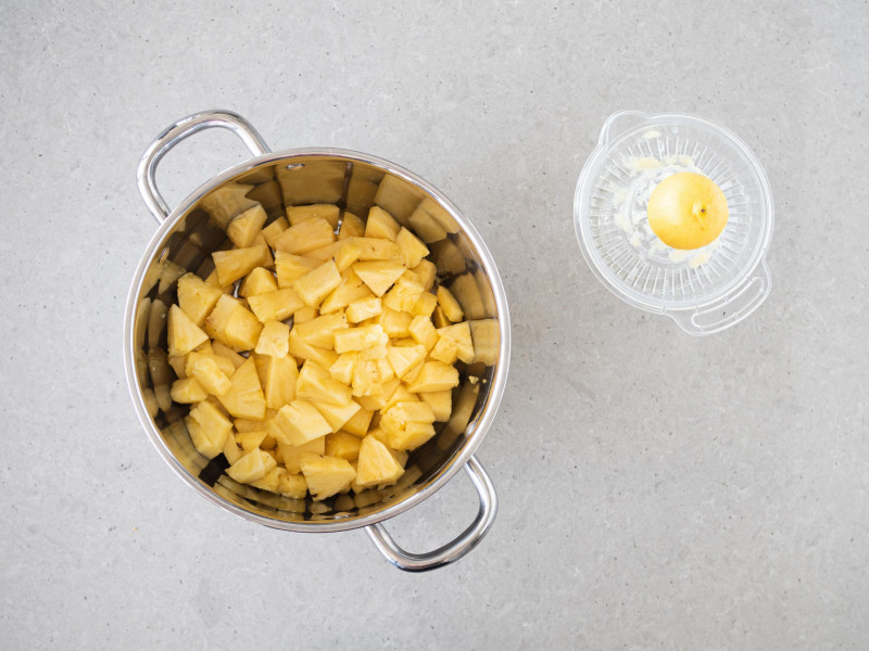 Pokrojony ananas w garnku. Obok sok z cytryny.
