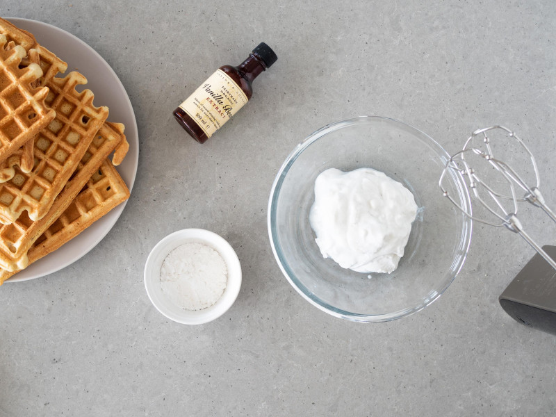 W miseczce śmietanka kokosowa. Obok cukier puder i ekstrakt z wanilii Taylor & Colledge. Na talerzyku usmażone gofry.