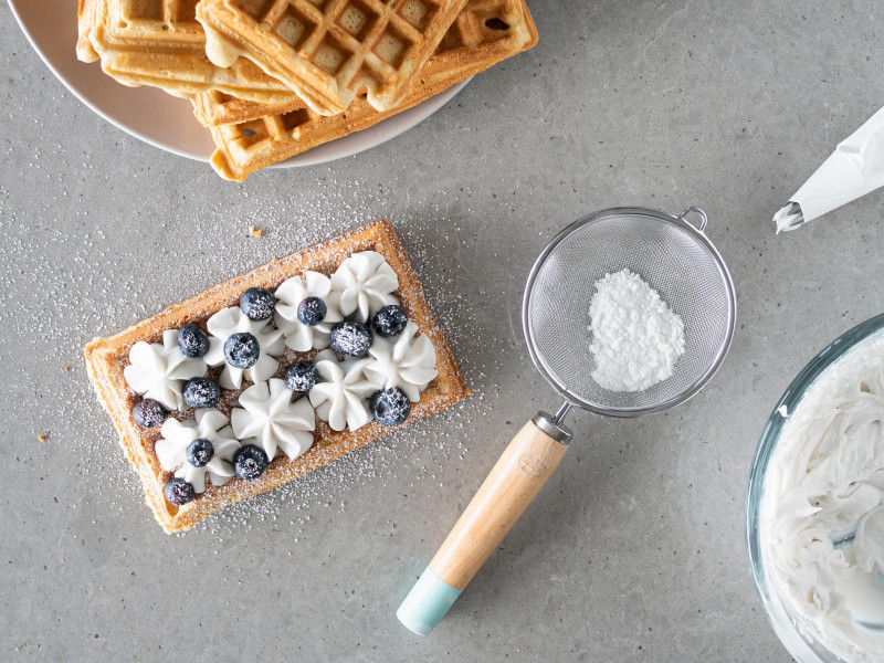 Wegański gofr z ubitą śmietanką kokosową i borówkami. Posypany cukrem pudrem.