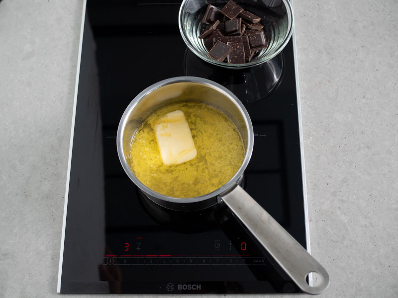 w rondelku rozpuszczone masło obok pokrojona czekolada w miseczce