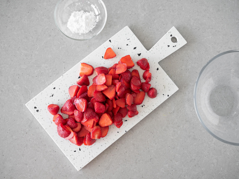 Na desce umyte i pokrojone w plastry truskawki. Obok w miseczce mąka ziemniaczana.