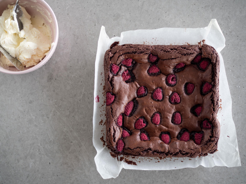na blacie brownie z malinami i kremem śmietankowym w miseczce