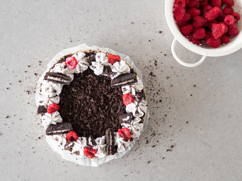 Udekorowany wegański sernik oreo z malinami i ubitą śmietanką kokosową.