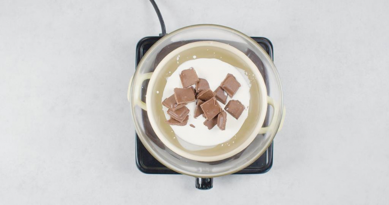 Czekolada mleczna i śmietanka w misce nad garnkiem w kąpieli wodnej