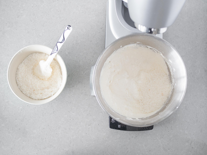 W misie robota kuchennego piana bezowa wymieszana z wiórkami kokosowymi. Obok w misie wiórki kokosowe.