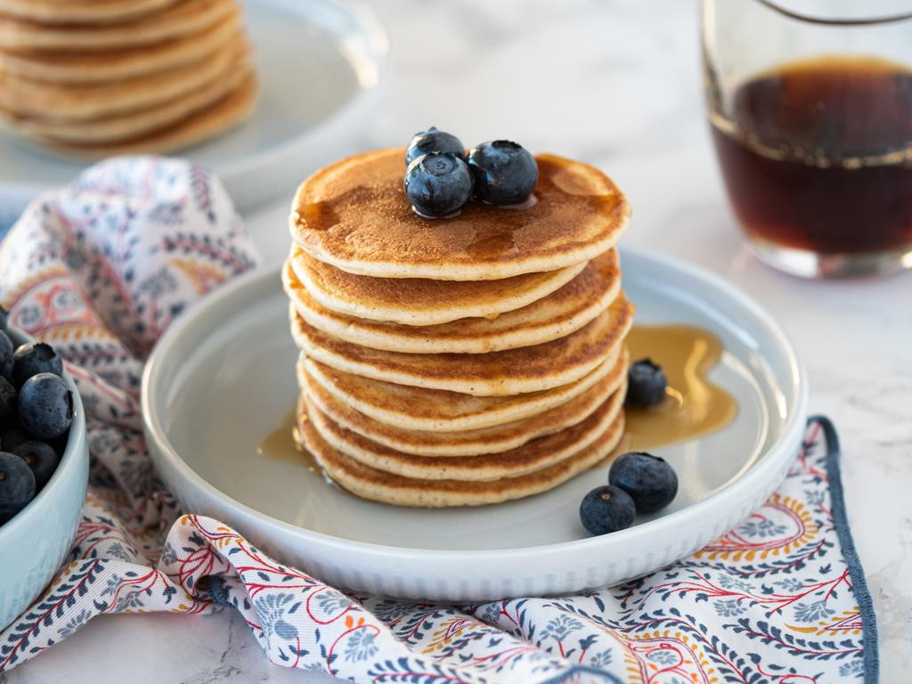 Puszyste pancakes (pankejki) polane syropem klonowym na talerzyku, udekorowane borówkami - Wszystkiego Słodkiego