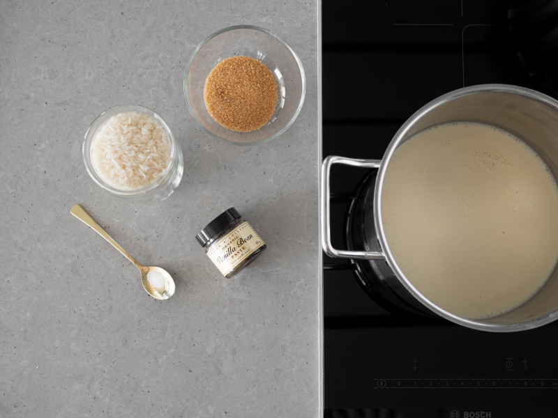 W garnku napój sojowy. Obok w miseczce cukier trzcinowy, ryż jaśminowy, pasta waniliowa taylor&colledge i szczypta soli.