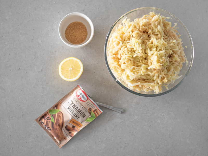 Starte jabłka w misce. Obok cukier trzcinowy, cytryna i cynamon mielony.