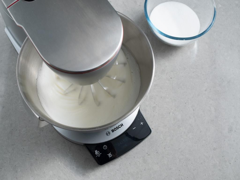 piana z białek w misie robota kuchennego bosch ubijana na bezę, obok miseczka z cukrem