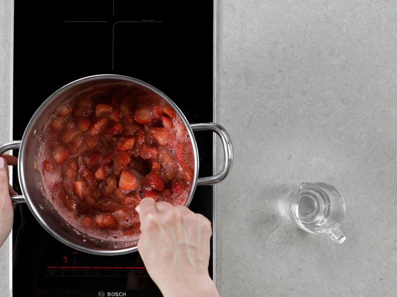 na płycie indukcyjnej dwupalnikowej bosch garnek z gotującym się rabarbarem i truskawkami