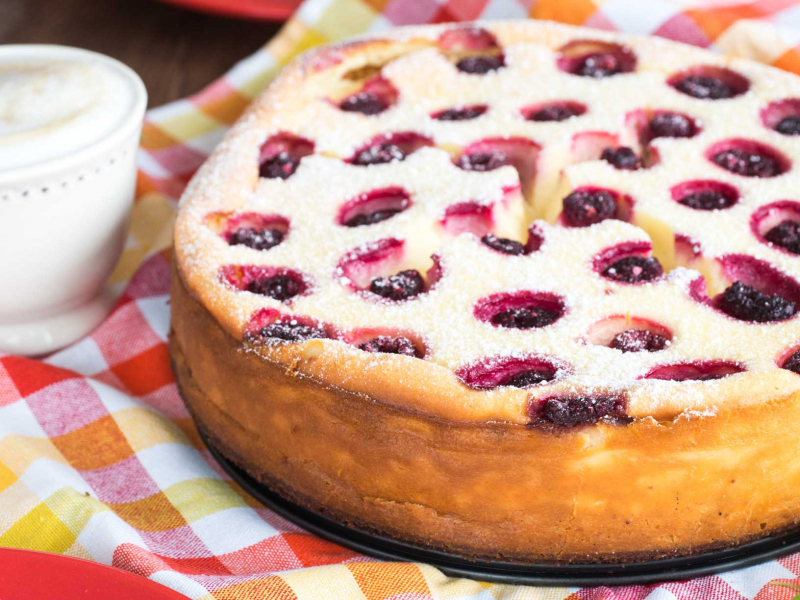 upieczony i posypany cukrem pudrem sernik z białą czekoladą i malinami na kakaowym ciasteczkowym spodzie