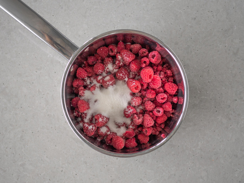 Maliny z wod膮 i cukrem w garnku.