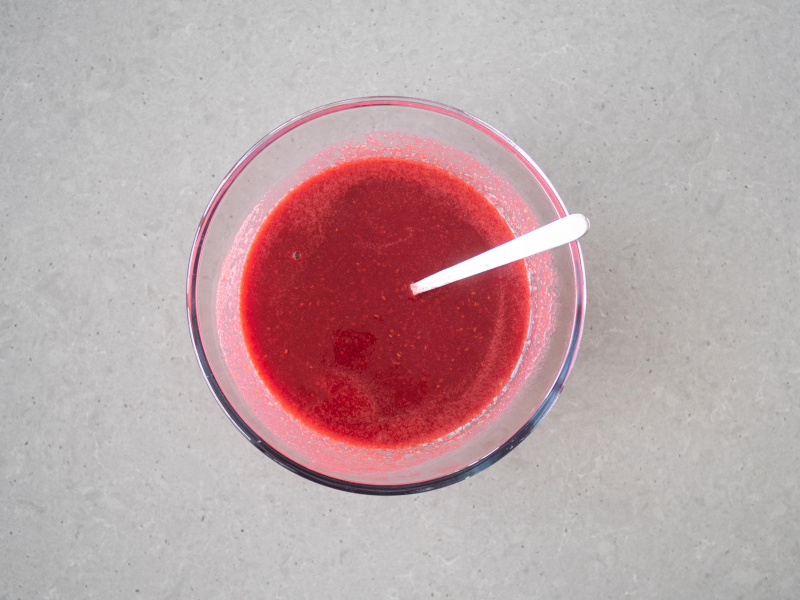 Zagotowane zblendowane maliny z agarem i cukrem w misce szklanej.