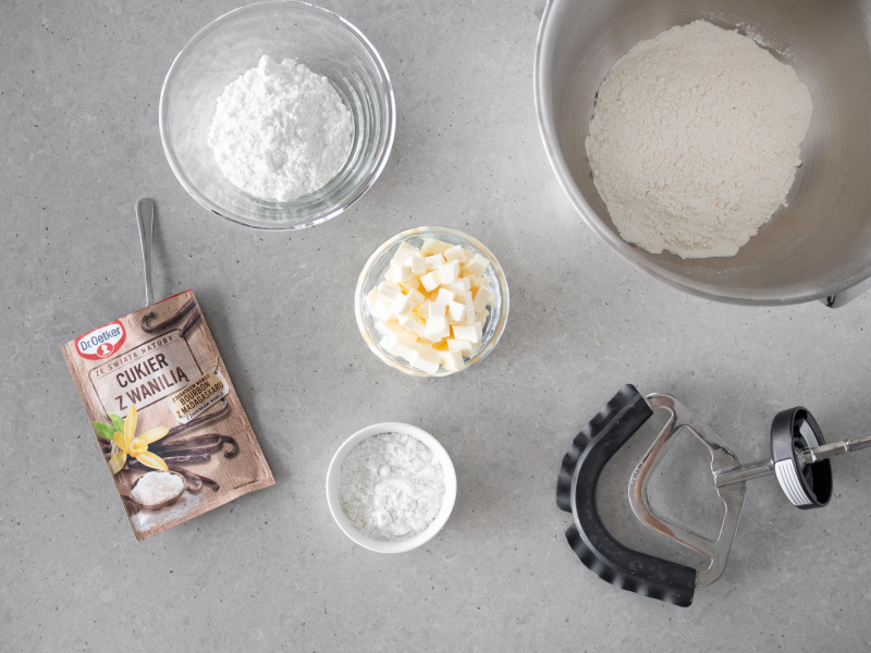 M膮ka pszenna w misie miksera. Obok w miseczce cukier puder, m膮ka ziemniaczana, olej kokosowy oraz opakowanie cukru z wanili膮 Dr. Oetkera.