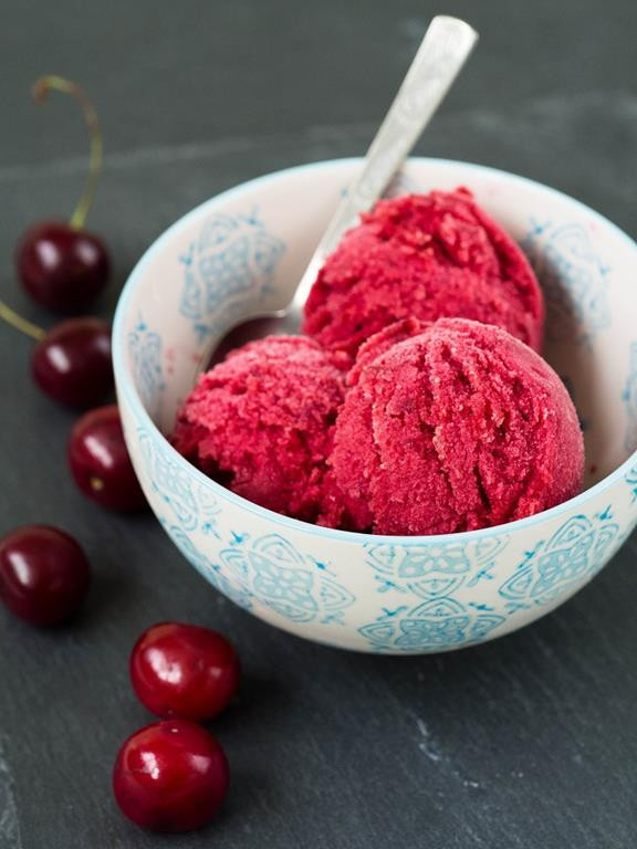 sorbet wiśniowy w miseczce z łyżeczką, obok rozsypane wiśnie - Wszystkiego Słodkiego