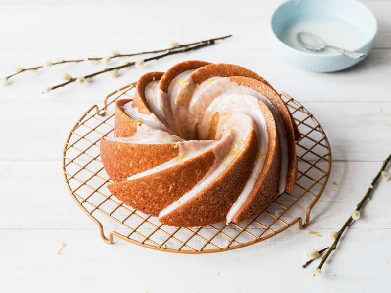 babka kokosowa udekorowana lukrem cytrynowym na kratce do studzenia, obok miseczka z lukrem