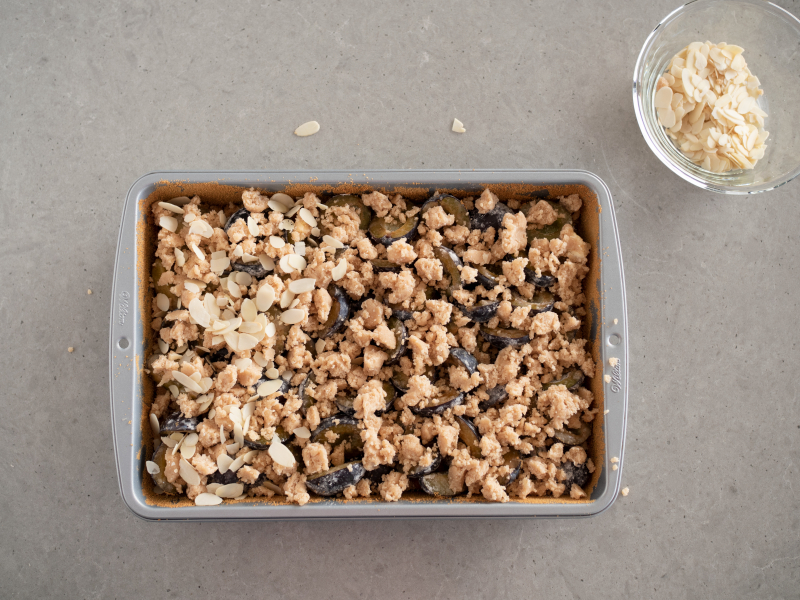 śliwki wyłożone na upieczony spód , płatki migdałów  pokruszone ciasto