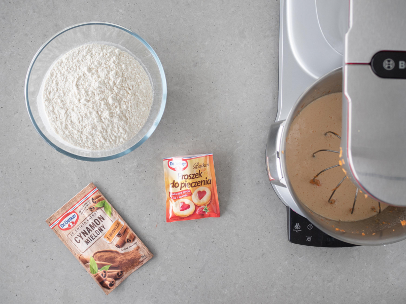 Na stole miska z mąką pszenną. Obok cynamon mielony i proszek do pieczenia firmy Dr. Oetker.