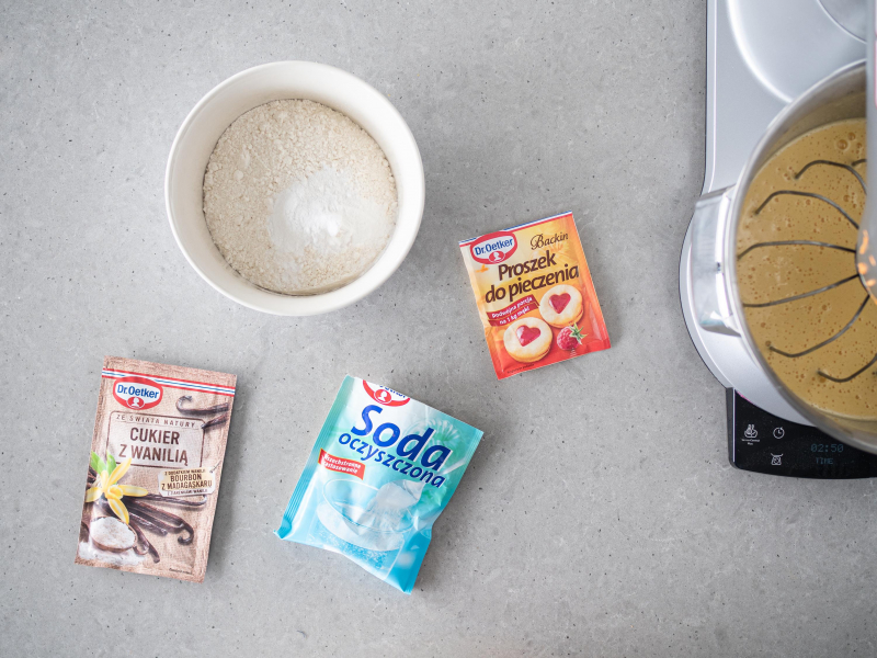 W ceramicznej misce mąka pszenna, obok proszek do pieczenia, soda i cukier z wanilią.