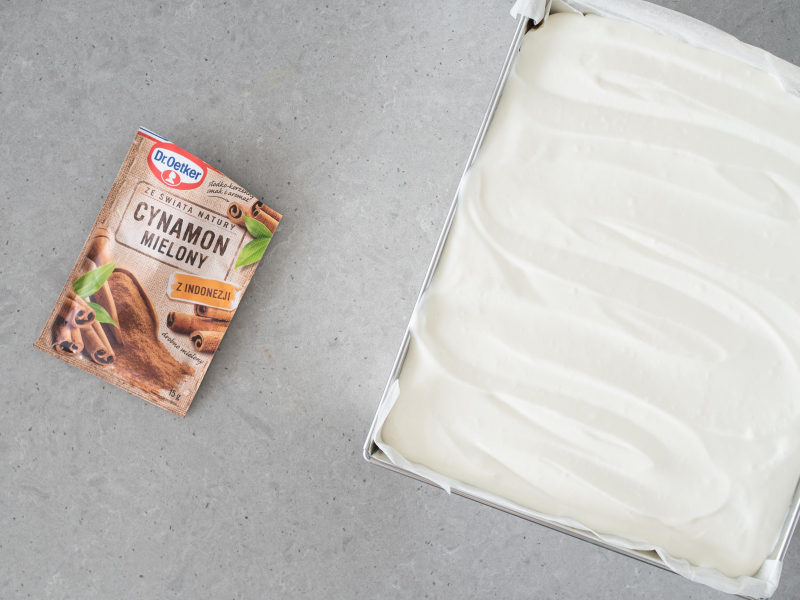 Krem rozsmarowany na cieście dyniowym. Obok cynamon mielony Dr. Oetkera.
