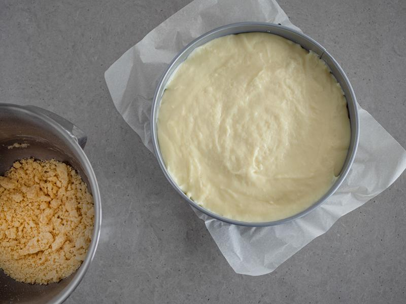 w tortownicy marki Wilton szarlotka z budyniem obok przygotowana w misce kruszonka