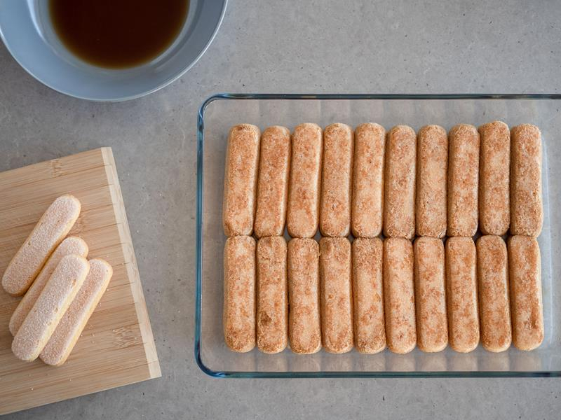 w szklanej prostokątnej formie żaroodpornej warstwa nasączonych w mieszance kawy z winem Marsala podłużnych biszkoptów Savoiardi do tiramisu