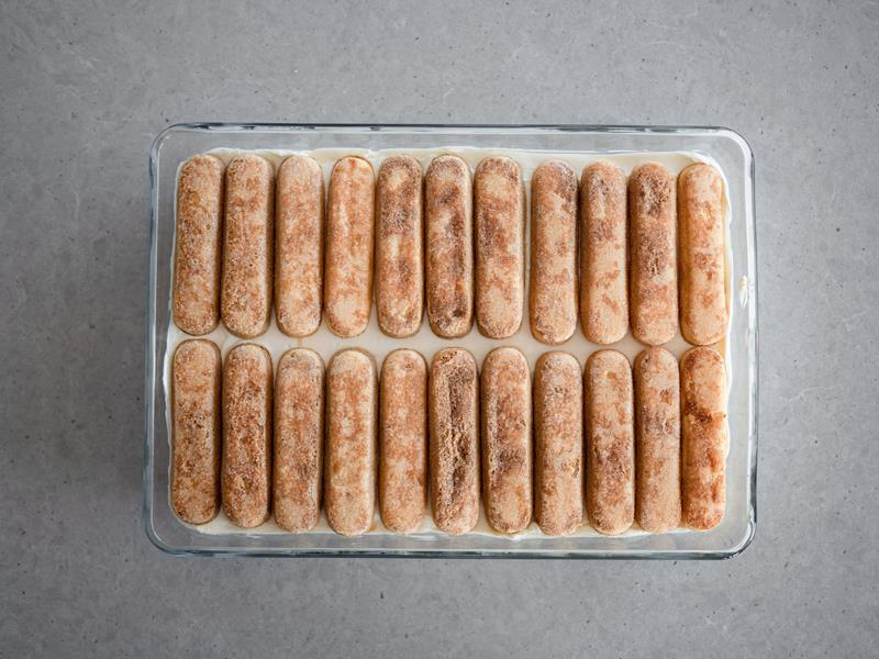 w szklanej prostokątnej formie żaroodpornej warstwa nasączonych w mieszance kawy z winem Marsala podłużnych biszkoptów Savoiardi, na nich warstwa kremu waniliowego oraz druga warstwa nasączonych biszkoptów