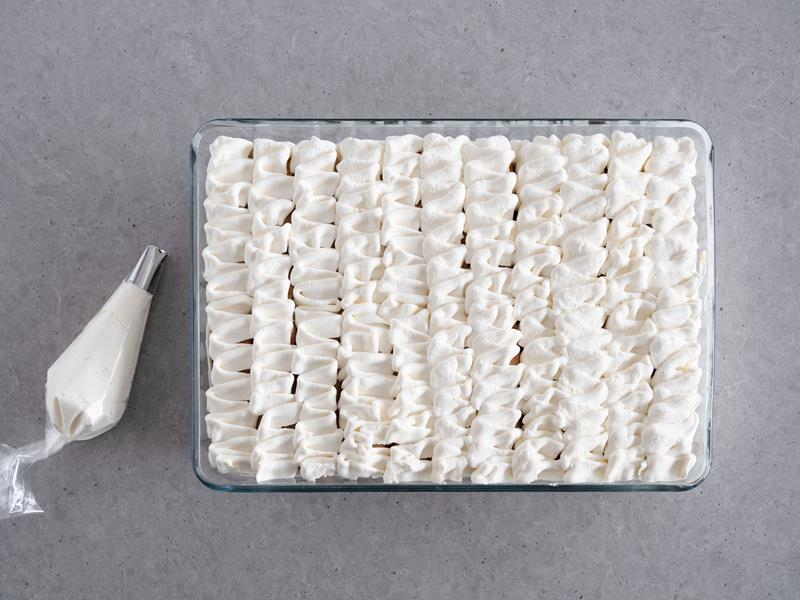 w dużej formie tiramisu bez żółtek udekorowane na wierzchu kremem waniliowym za pomocą worka cukierniczego z ozdobną końcówką