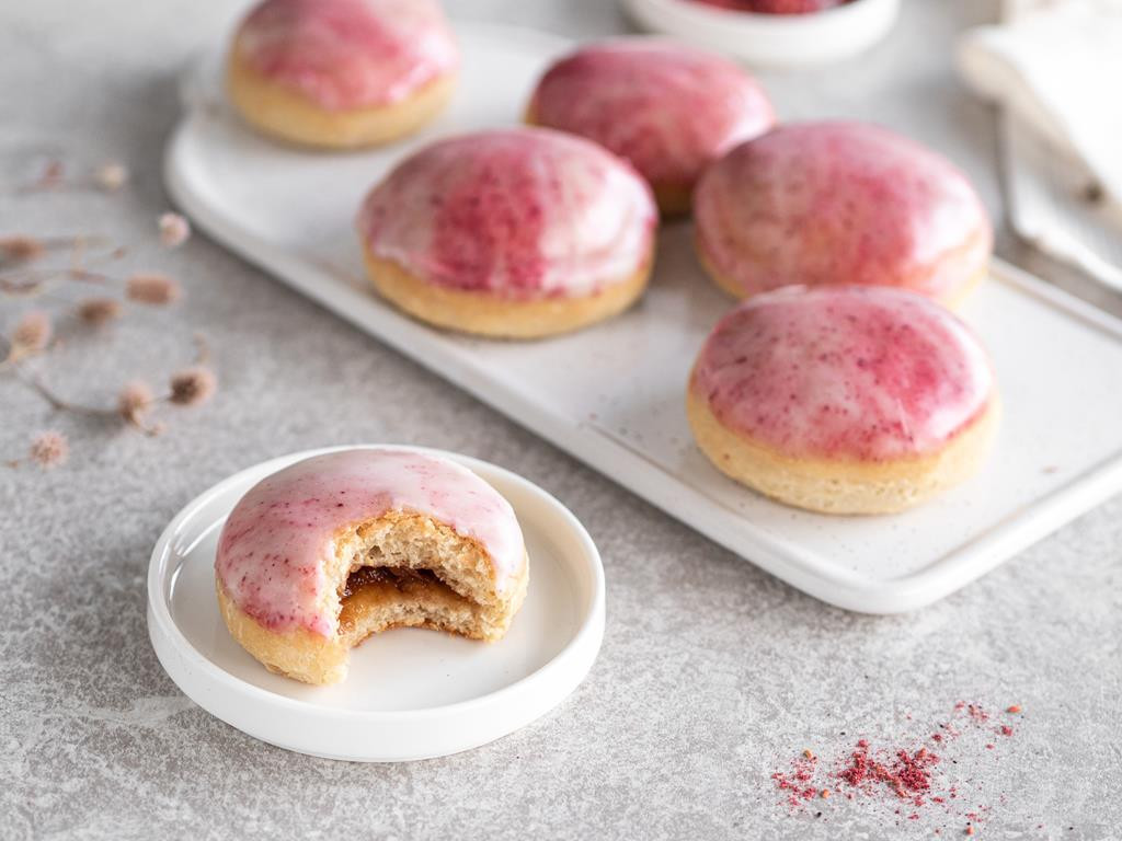 wegańskie pączki pieczone z różaną marmoladą, dwukolorowym różowym, marmurkowym lukrem na białej desce.