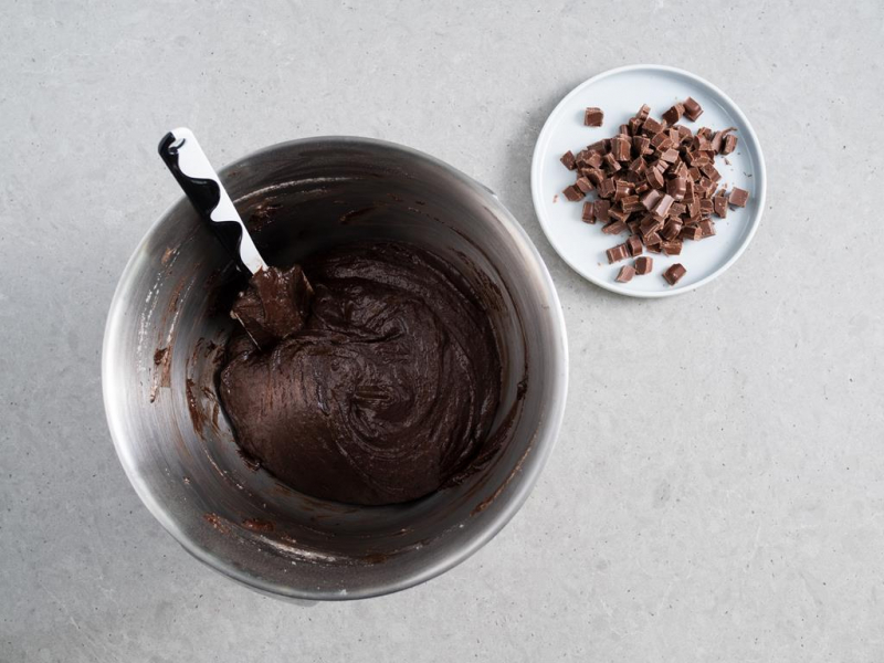 ciasto kakaowe na babkę-czaszkę w misie robota kuchennego z silikonową szpatułką, obok czekolada mleczna pokrojona w kosteczkę na talerzyku