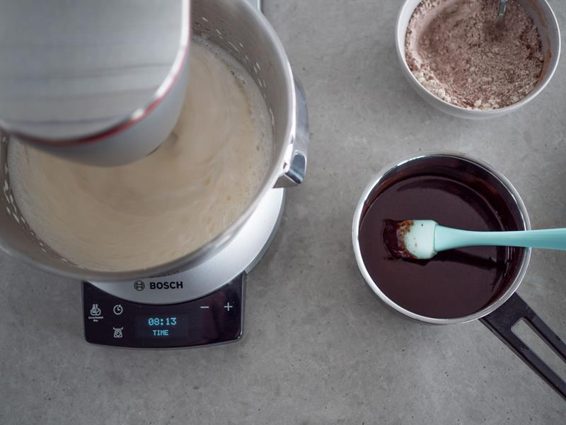 w misie robota kuchennego bosch jajka ubite z cukrem na biały puch, obok w rondelku rozpuszczona z masłem czekolada oraz w miseczce mąka przesiana z proszkiem do pieczenia i kakao