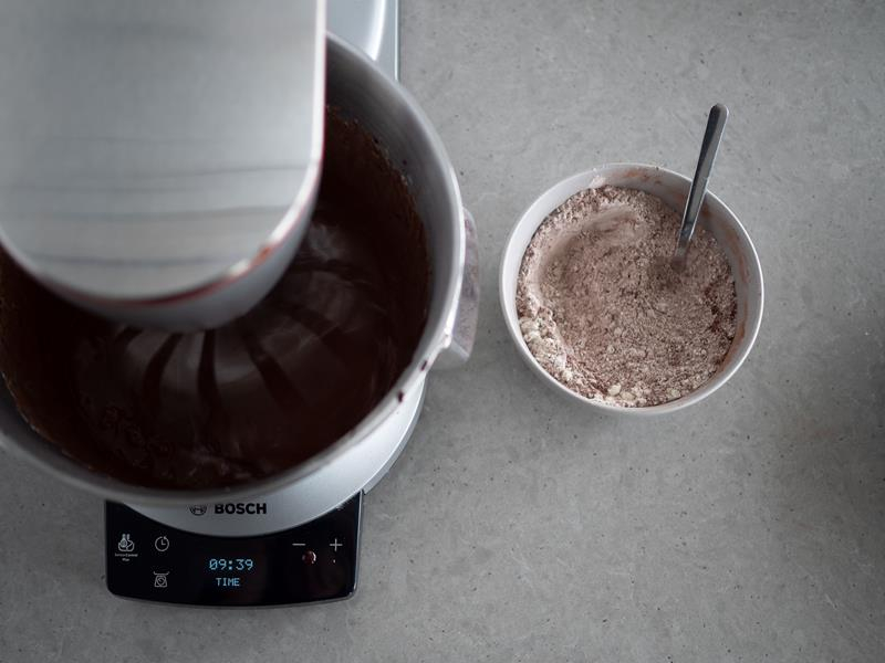 w robocie kuchennym bosch masa na ciasto czekoladowe przed wymieszaniem z suchymi składnikami stojącymi obok w miseczce
