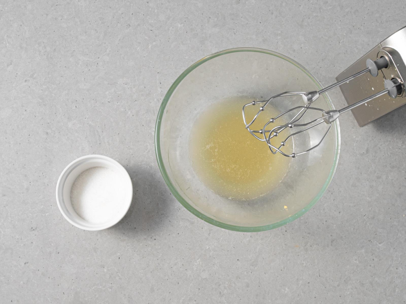 Aquafaba w szklanej misce. Obok cukier w małej miseczce.