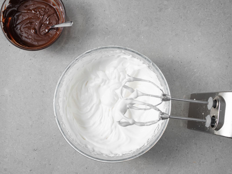 Ubita z cukrem aquafaba w szklanej misce. Obok rozpuszczona czekolada w miseczce.