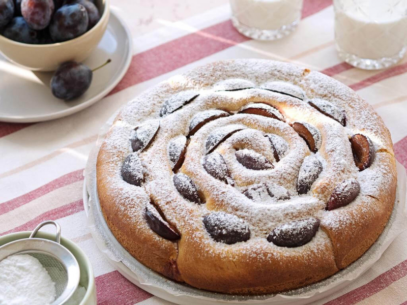 Drożdżówka zawijana z twarogiem i śliwkami posypana cukrem pudrem i podana na paterze - Wszystkiego Słodkiego