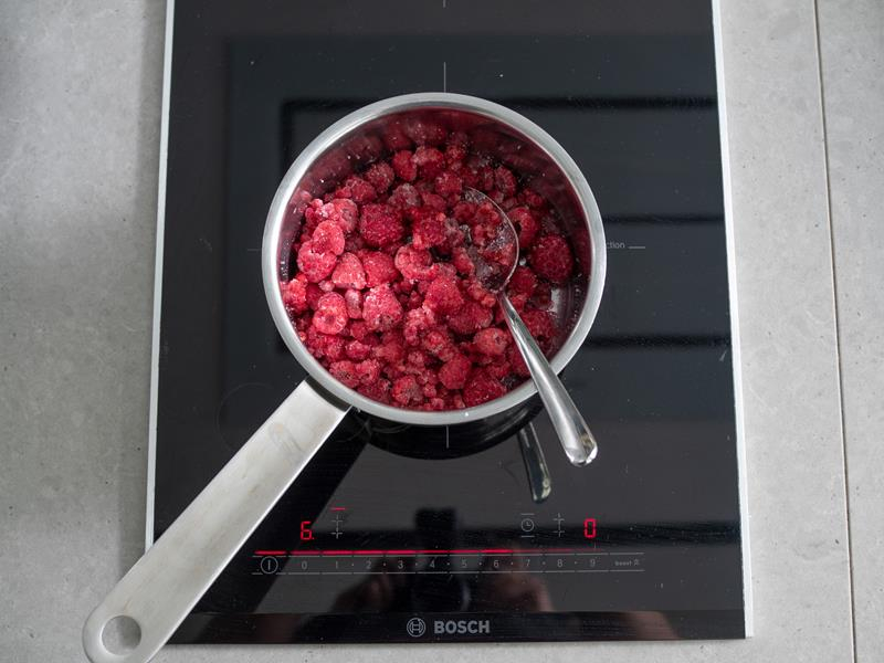 mrożone maliny w rondelku z łyżką na płycie kuchenki