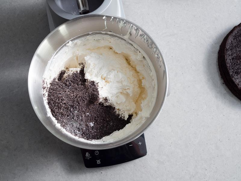 śmietanka ubita z cukrem pudrem i śmietan-fixem w misie robota kuchennego oraz dosypane do niej pokruszone ciasteczka oreo
