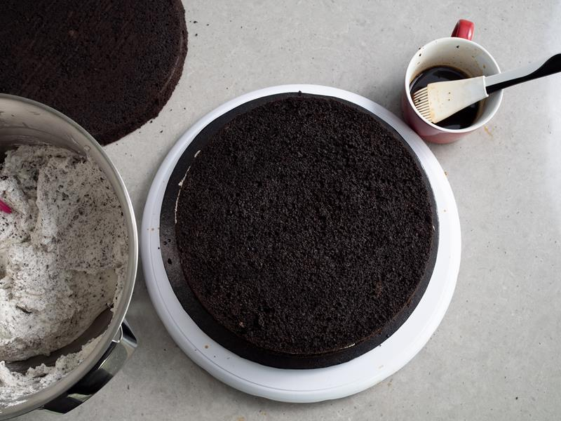 drugi blat biszkoptu wyłożony na warstwę kremu, kubek z kawą i pędzelkiem do nasączenia, misa z kremem oraz trzeci blat biszkoptu