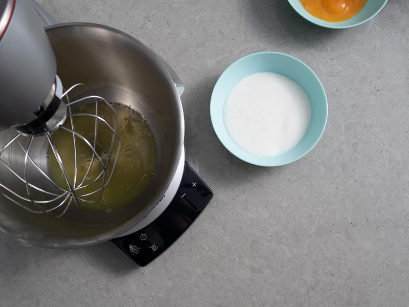 białka jaj w misie robota kuchennego, obok miseczka z cukrem oraz miseczka z żółtkami