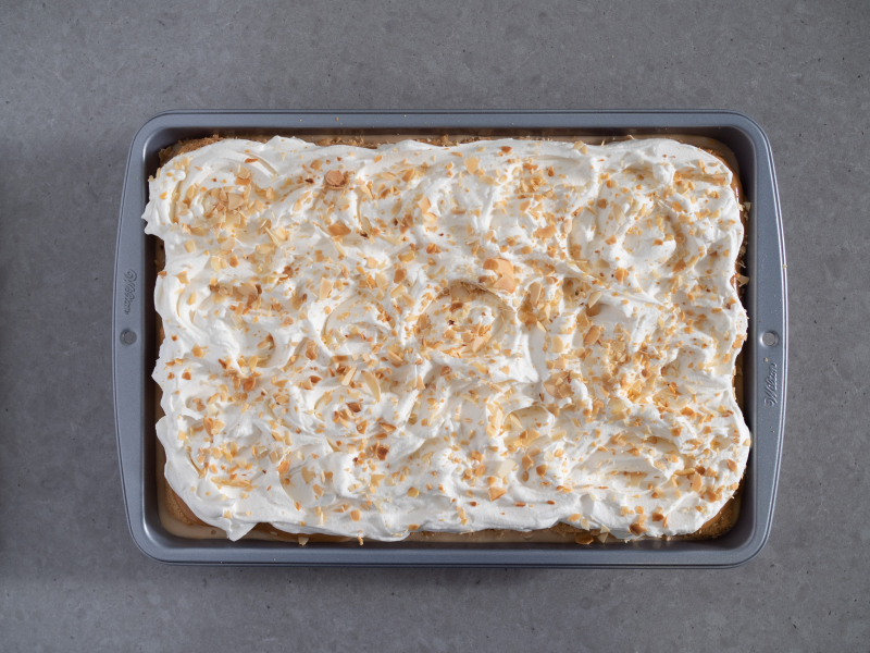 ciasto krówka przykryte ubitą śmietanką i posypane uprażonymi płatkami migdałów