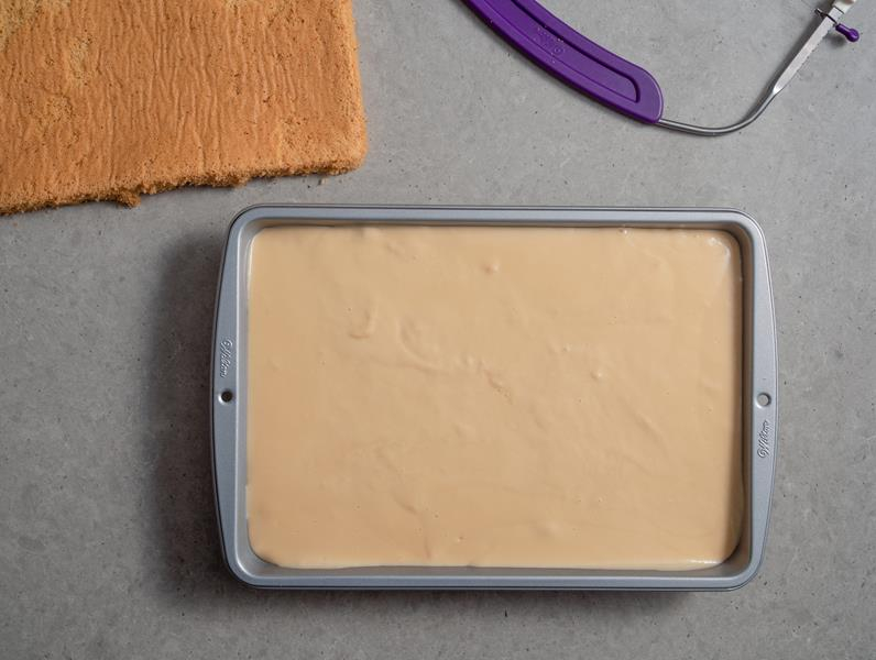 w formie wilton pierwszy blat biszkoptu zalany kremem budyniowym toffi, obok drugi blat biszkoptu oraz nóż strunowy wilton