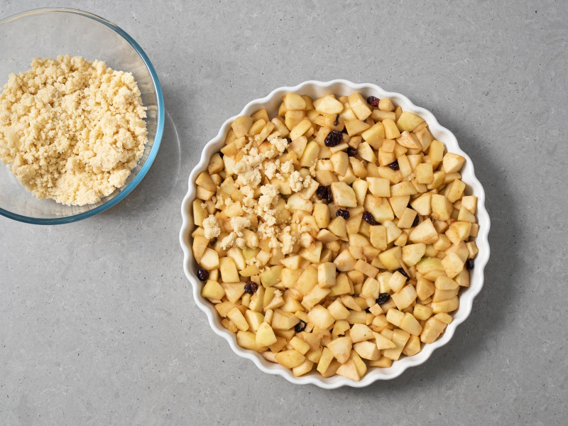 podprażone jabłka przełożone do formy ceramicznej, obok kruszonka w misce