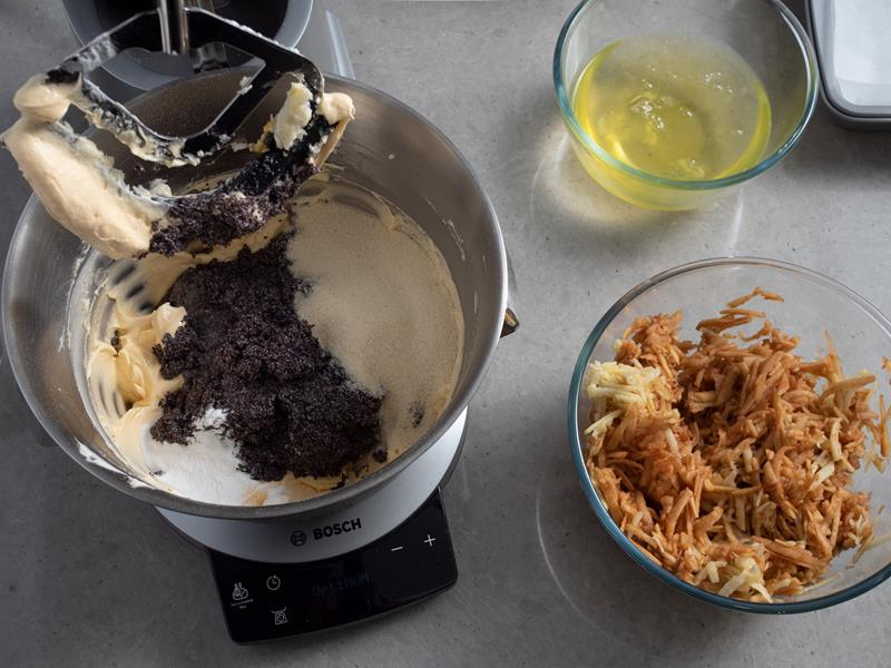 dodawanie maku do misy robota kuchennego bosch z masłem utartym z cukrem i żółtkami, obok miska ze startymi jabłkami oraz miseczka z białkami jaj