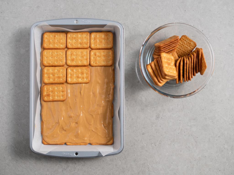 masa kajmakowa rozsmarowana na warstwie krakersów, obok miseczka z krakersami