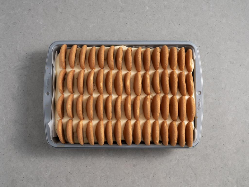 biszkopty podzielone na połówki i ułożone pionowo na kremie budyniowym