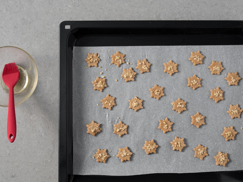 Ciastka korzenne posmarowane białkiem i posypane orzechami.